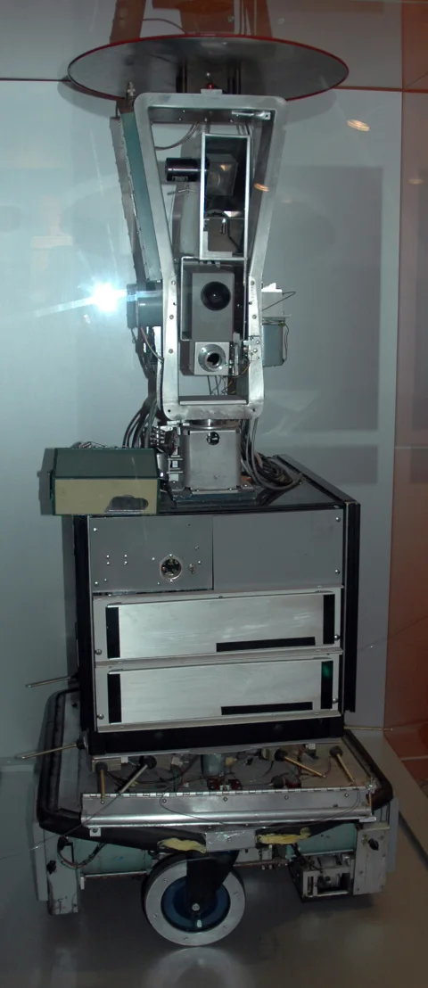 Shakey behind glass: stacked white and black equipment housings rise above a circular wheeled base.